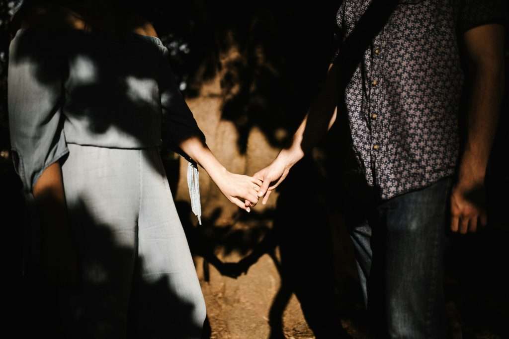 Two people holding hands, faces out of frame, in dappled shade