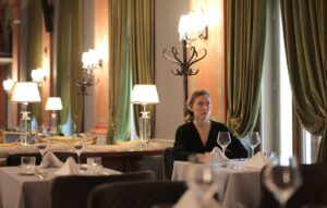 Woman in a black top sitting alone at an elegant restaurant table, looking away from the camera