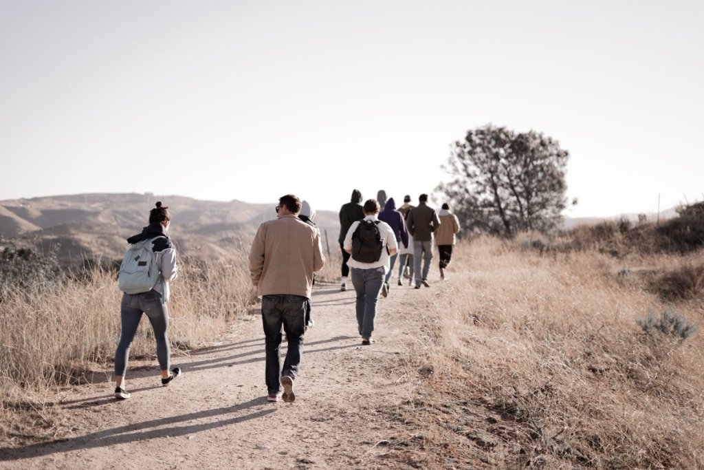 A group of adults hiking together along a dirt trail through dry golden hills