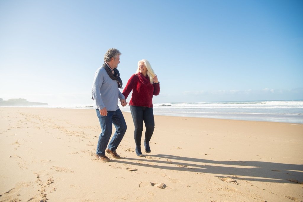 A couple in their sixties walking hand in hand along a beach