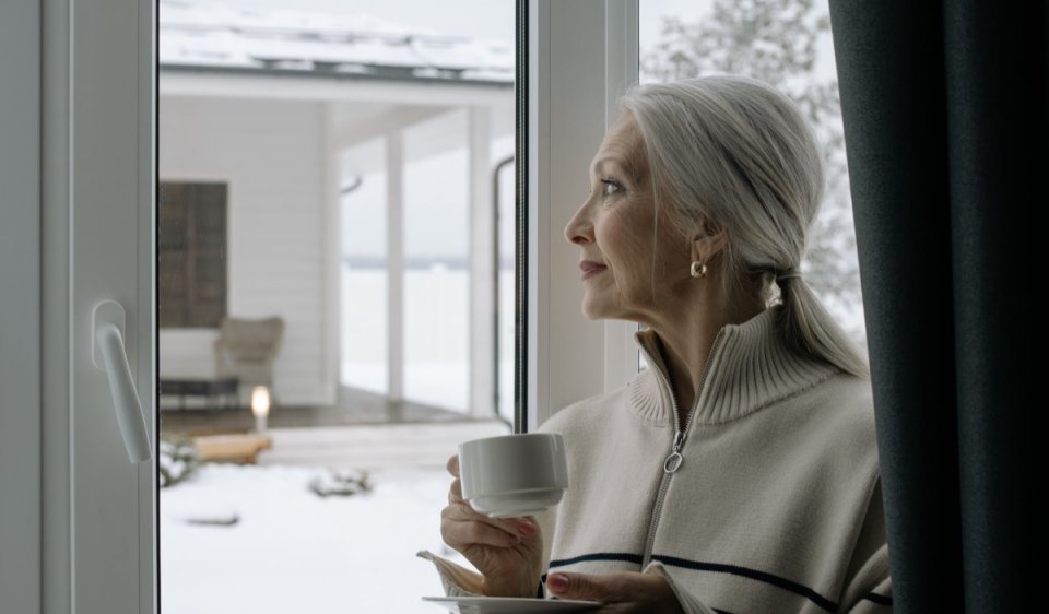 A woman with a cup of coffee looking out of a window, thinking something over